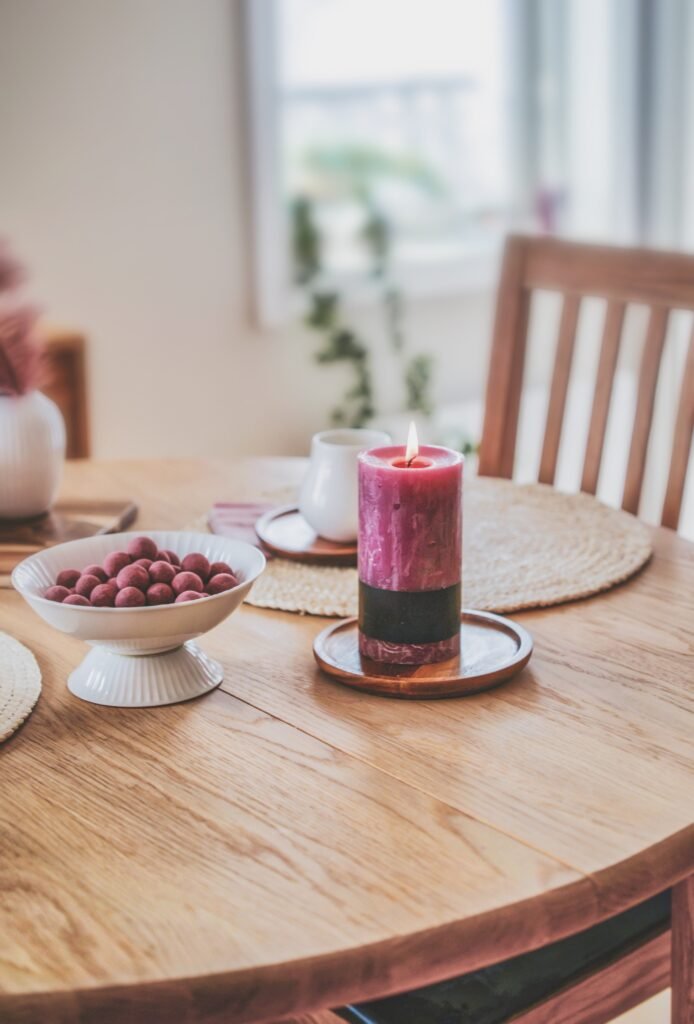 Mesa de madeira com vela acesa, chávena de café e taça de frutos vermelhos num ambiente acolhedor
