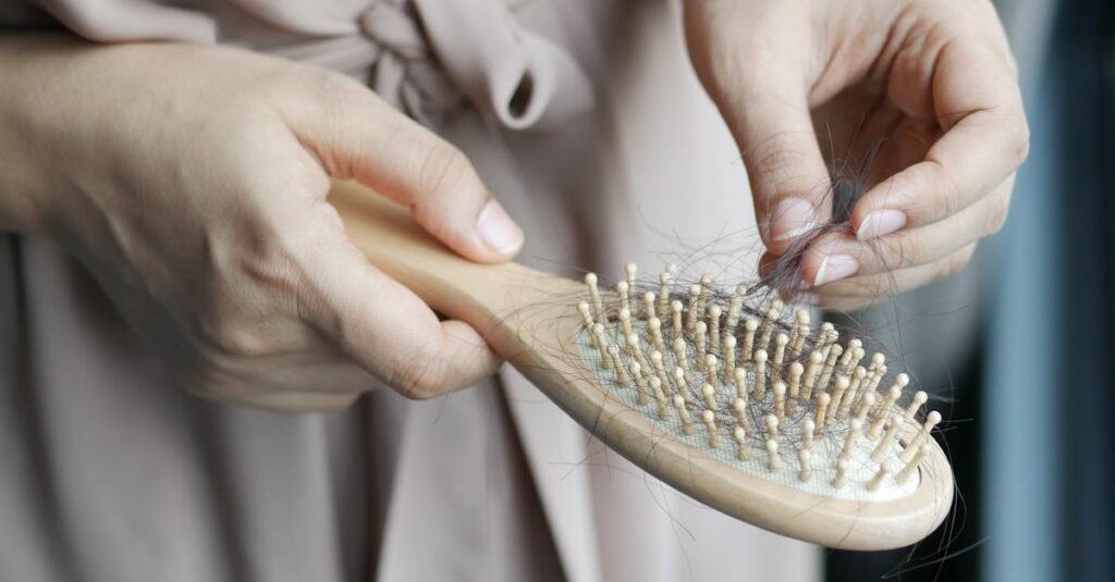 Close-up image of hands removing hair from a wooden brush, emphasizing daily hair care routine.