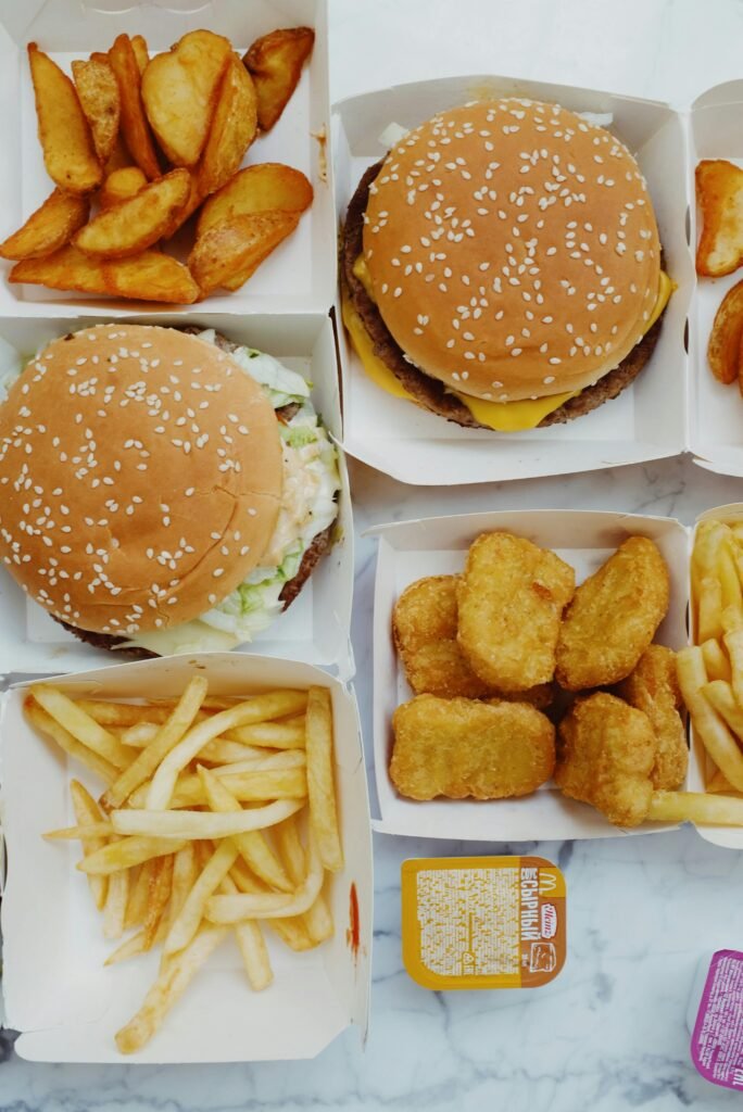 Vista superior de comida rápida com hambúrgueres, batatas fritas e nuggets, ilustrando hábitos alimentares que podem contribuir para dificuldades de concentração e menor clareza mental.