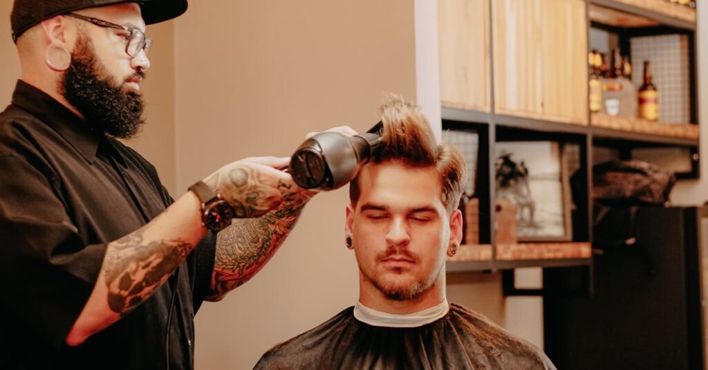 Queda de cabelo: 5 causas que podem estar por trás? 13 Side view of informal tattooed bearded male barber blow drying hair of stylish customer in modern salon