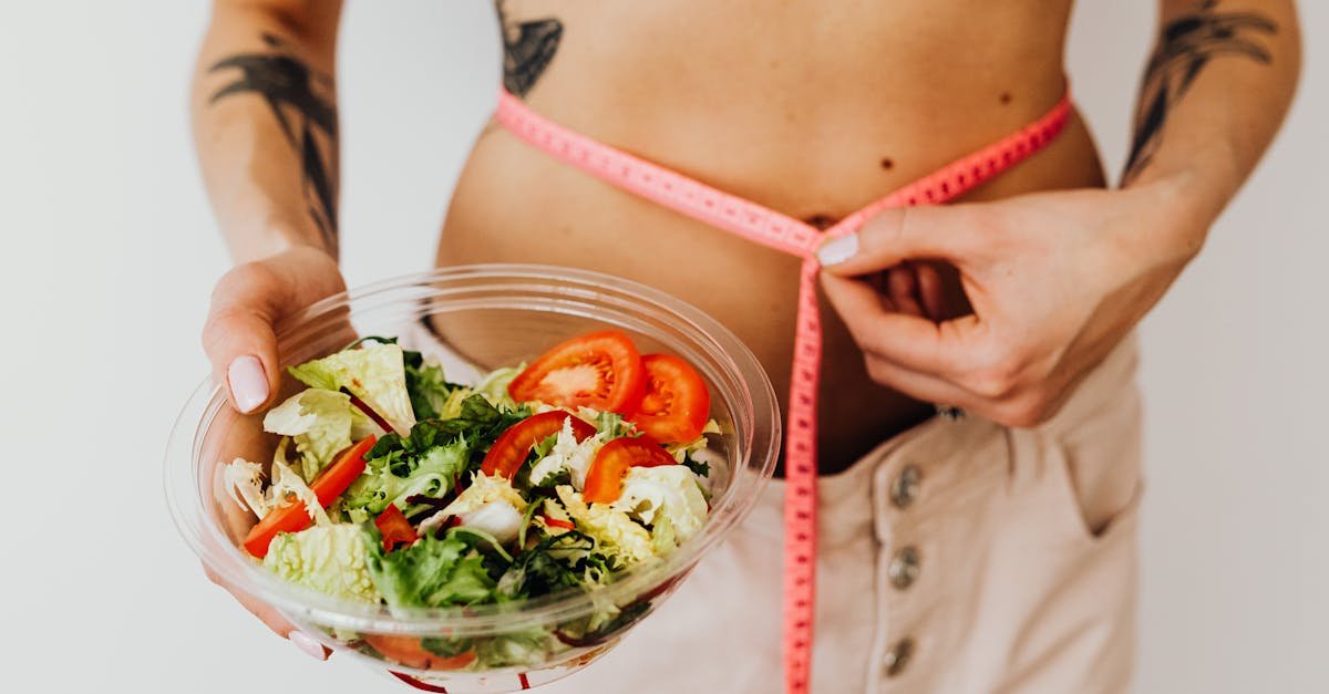 9 mitos sobre nutrição em que você ainda acredita 1 Mulher a medir a cintura com fita métrica enquanto segura prato com salada, ilustrando mitos sobre nutrição e controlo alimentar