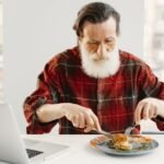 Ferro baixo sem anemia: 6 sinais a observar 6 Homem a comer sozinho enquanto trabalha no computador, possível ferro baixo sem anemia e sensação de cansaço