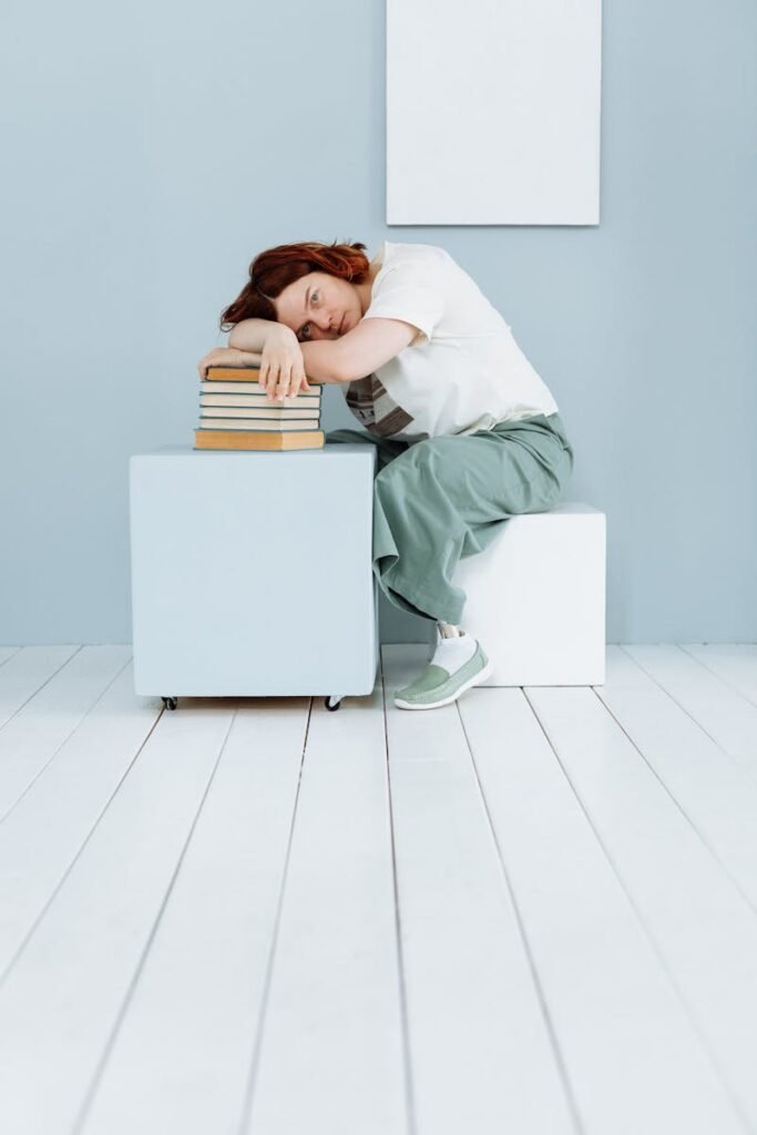Ferro baixo sem anemia: 6 sinais a observar 11 Woman resting her head on books in a minimalist setting, symbolizing exhaustion and stress.