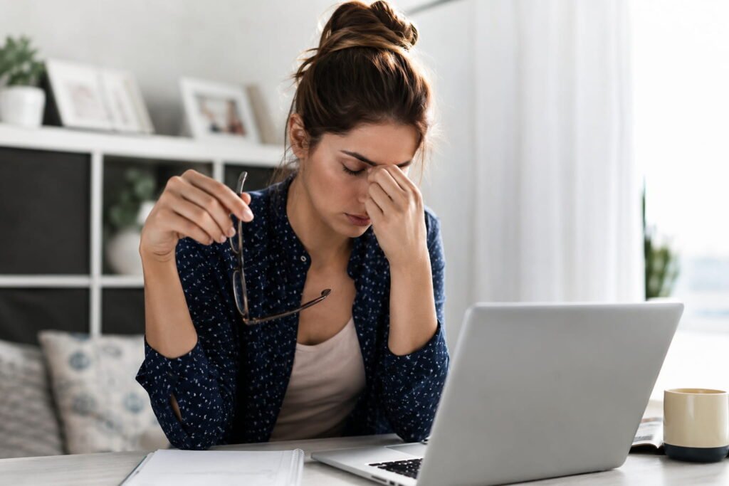 Mulher com expressão cansada ao computador representando fadiga adrenal e stress crónico